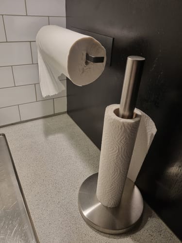 Kundes selvklebende tørkerullholder montert på veggen over en tørkerullholder som står på kjøkkenbenken.