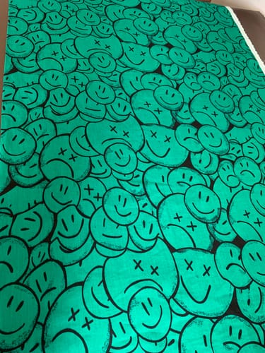 Customer's green cotton lawn fabric laid flat, showing a pattern of black-outlined happy and sad smiley faces.