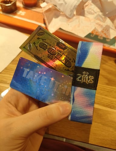 Customer holding a colorful ZOX bracelet, a galaxy-themed card, and a gold First Edition card from their Mystery Club+.