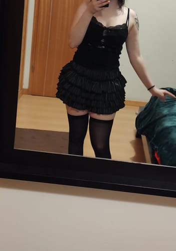Reviewer in a mirror selfie wearing black, thigh-high Babygirl Basic Opaque Stockings with a ruffled skort.