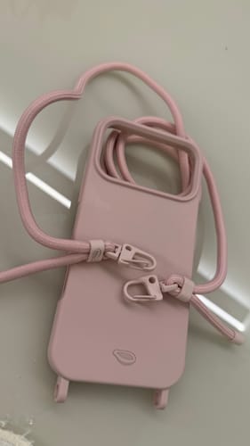 Foto de cliente da case Nora rosa com sua alça fina e prendedores, em uma superfície clara.