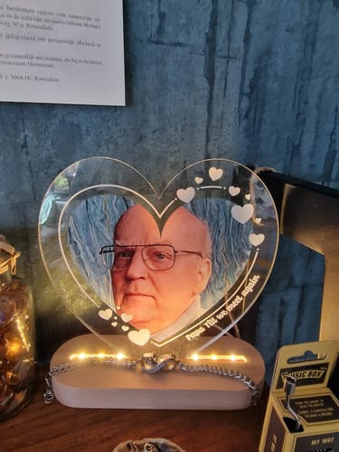 Recensent toont de verlichte, hartvormige ledlamp met een persoonlijke foto en gravure op een houten voet.