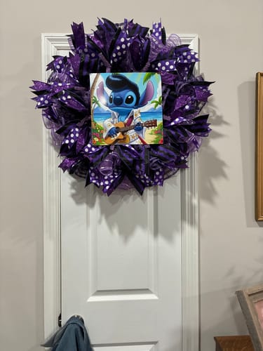 Reviewer's completed purple pancake wreath with polka-dot ribbons and a Stitch sign, hanging on a white door.