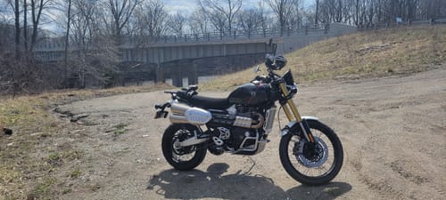 Customer's motorcycle with the Wind Rider Seat Cover installed, parked on a dirt road with a bridge in the background.