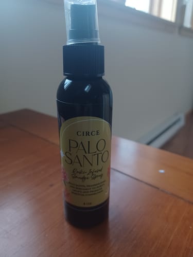 Customer's dark bottle of Palo Santo Spray standing on a wooden surface.