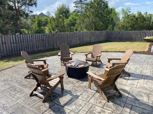 Reviewer's six brown Folding Adirondack Chairs arranged around a fire pit on a backyard patio.