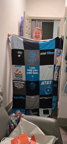 Reviewer happily holding up their custom Project Repat T-Shirt Quilt made from various AT&T t-shirts.