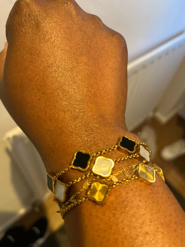 Close-up of a customer wearing three stacked Celine Clover Bracelets with black, white, and gold clover charms on their wrist.