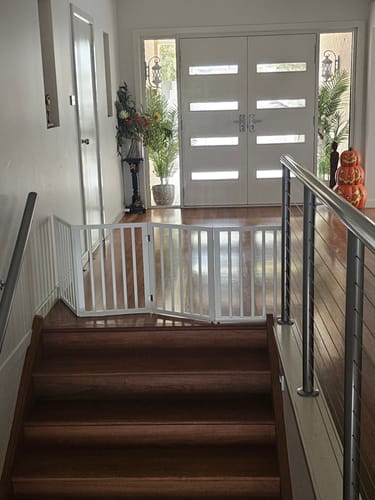 Customer's white foldable pet gate blocking the top of a wooden staircase in a hallway.