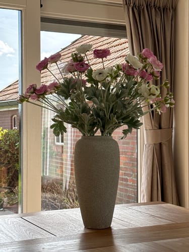 Recensent toont het Ranonkel Arrangement in een grote, grijze vaas op een tafel.