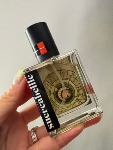Reviewer holds the square bottle of The Moon Door perfume, showing the intricate label design.