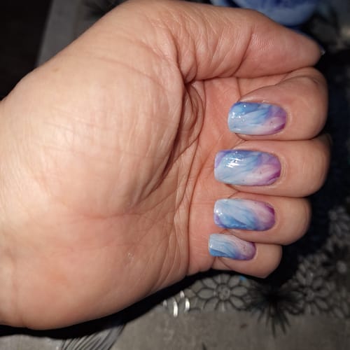 Nahaufnahme der Hand einer Kundin, die UV-Gel-Nagelfolien mit einem blau-lila marmorierten Muster trägt.