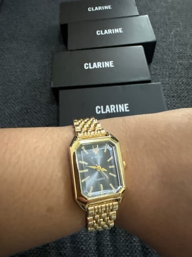 Customer wearing their gold CLAIRE DE MAINS watch on their wrist, with four black Clarine boxes visible in the background.