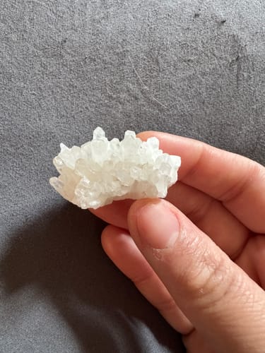 Customer holding a small, white crystal cluster in their hand against a grey surface.