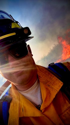 Customer wearing the LED Headlamp 2.0 on a wildland helmet with a fire in the background.