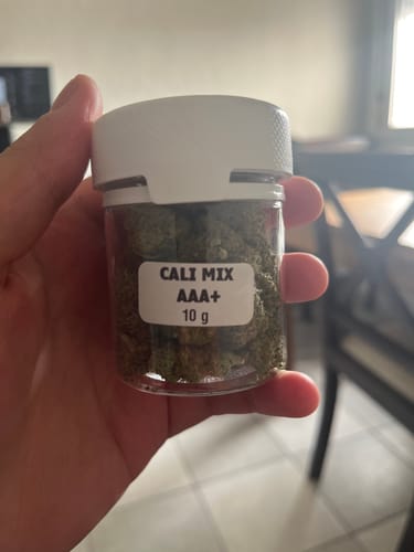 Customer holds a small, clear 10g jar of CALI MIX AAA+, showing the green flower buds inside.