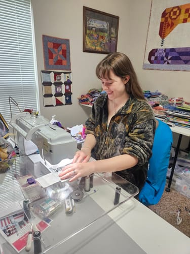 Customer sewing the floral and white precut squares from the Brick Prairie Precut Quilt Kit on a sewing machine.