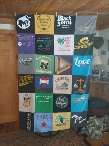 Customer's colorful Project Repat T-Shirt Quilt hanging in a room, displaying squares from numerous t-shirts with unique logos.