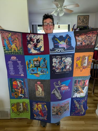 Customer holding up their Project Repat T-Shirt Quilt made from colorful Saratoga Jazz Festival t-shirts.