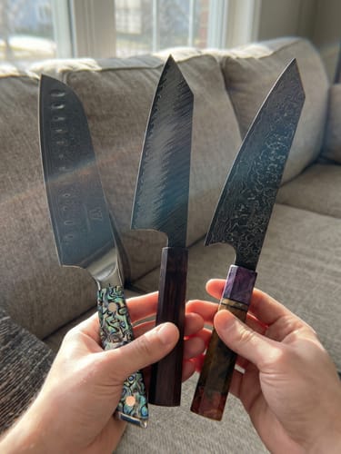 Ein Kunde hält drei hochwertige Küchenmesser aus der Mystery Box mit einzigartigen Griffen und gemusterten Klingen in der Hand.