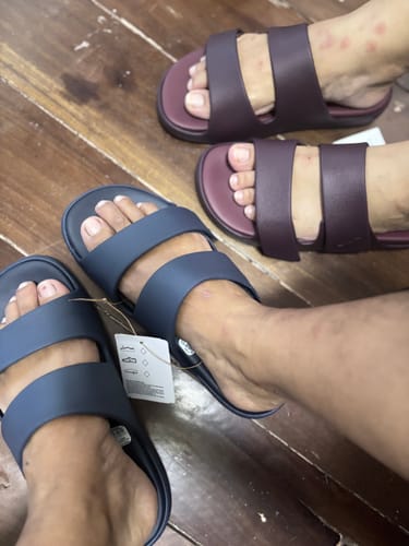 Customer wearing the blue adidas ZNSORY Sandals, with another person wearing the maroon pair on a wood floor.