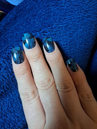 Kundenhand mit aufgetragenen 'Teal Foliage' UV-Gel-Folien. Die kurzen Nägel zeigen ein dunkles, blaugrünes Blattdesign.