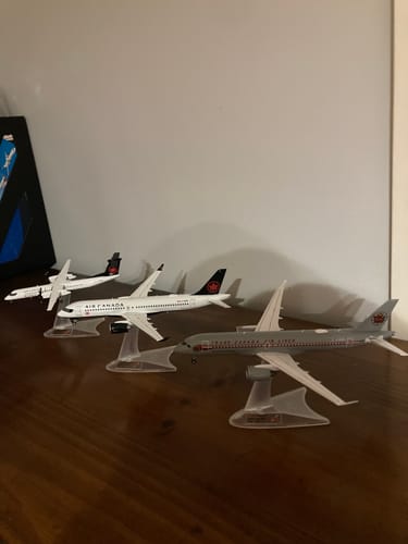 Customer's Air Canada A220-300 retro model displayed on a stand with three other model airplanes on a wooden surface.