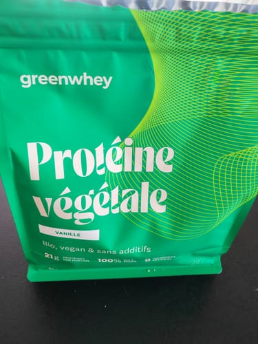 Photo d'un client du sachet vert de Protéine végétale, saveur vanille, posé sur une surface sombre.