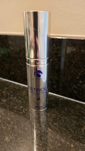 Customer's silver bottle of iS Clinical Retinol+ Emulsion 0.3 standing on a dark countertop.