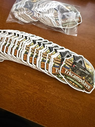 Customer's custom vinyl stickers with a white border and camping graphic, fanned out on a wooden table.