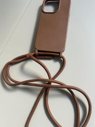 Cliente mostrando a Case Mocha Mousse com sua alça de corda da mesma cor sobre uma superfície branca.