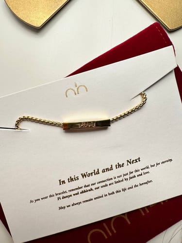 Customer's gold In This World and the Next Bracelet with an engraved bar, displayed on its presentation card.