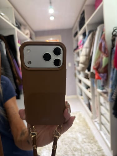 Cliente segurando um celular com a Cordinha Nora Mocha Mousse, mostrando os ganchos dourados.