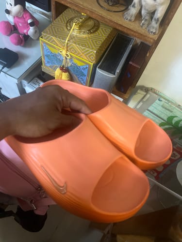 Customer holding a pair of orange Nike Men's ReactX Rejuven8 Slides in their hand.