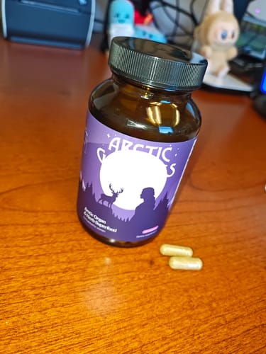 Customer's bottle of Reindeer Organ Superfood and two capsules resting on a wooden desk.