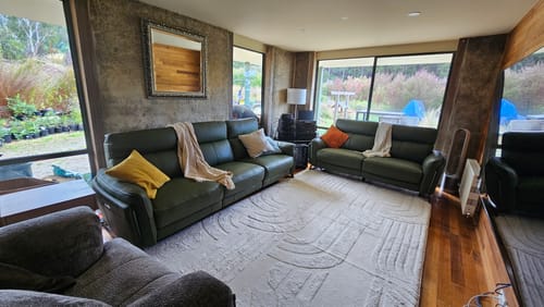 Customer's large Vanilla Cream Mellow Mat on a wooden floor in a living room between two dark green sofas.