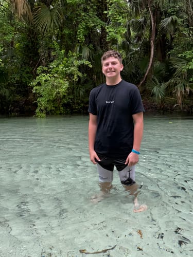 A reviewer wearing the black SAVD Performance T-Shirt while standing in clear water outdoors.