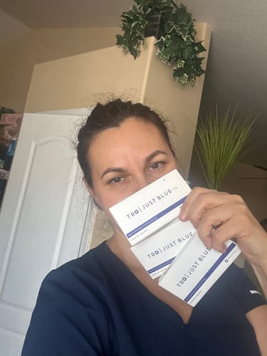 Reviewer holding three white boxes of Just Blue™ close to the camera, partially obscuring their face.