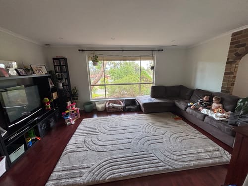 A reviewer's large, light-colored Mellow Mat with a carved design, spread across a living room floor with children on a couch.