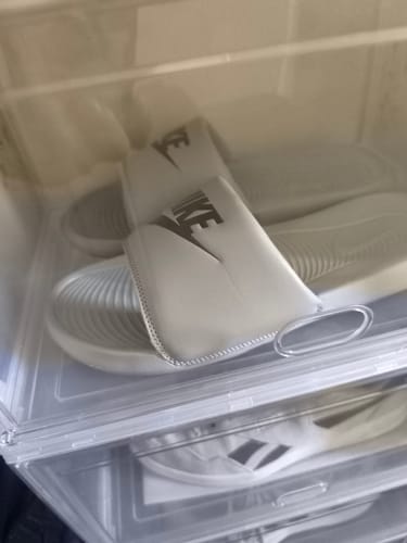 Customer's light-colored Nike Men's Victori One Slides inside a clear plastic shoebox.