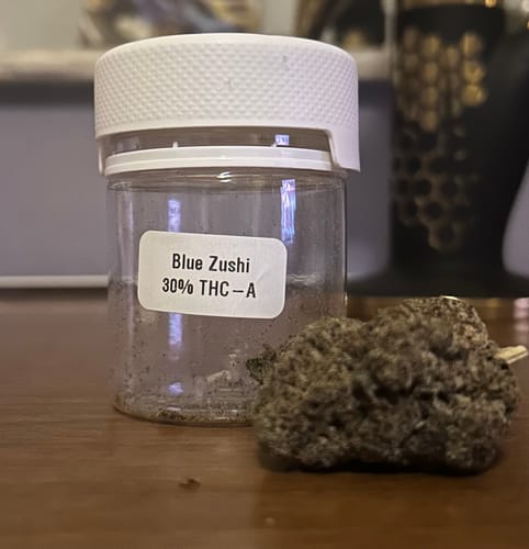 Customer's dense Blue Zushi bud displayed next to its empty labeled jar on a wooden surface.
