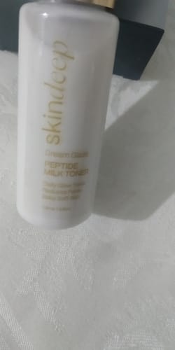 Partial view: Reviewer's white Dream Glaze Peptide Milk Toner bottle with gold lettering on a white surface.