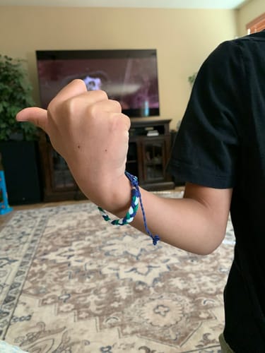 Customer wearing the woven blue, green, and white DAVID Bracelet on their wrist indoors.