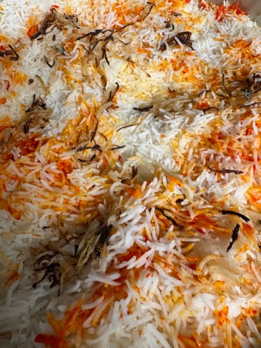 Customer's close-up of a colorful rice dish made with Halal Veal Cubes, topped with fried onions.