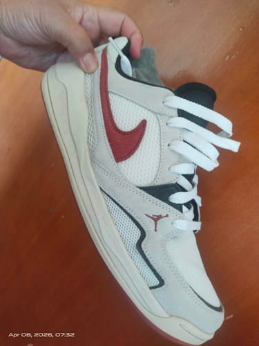 Customer holding a single Jordan CMFT Era casual shoe, showing its off-white body, red swoosh, and black accents.