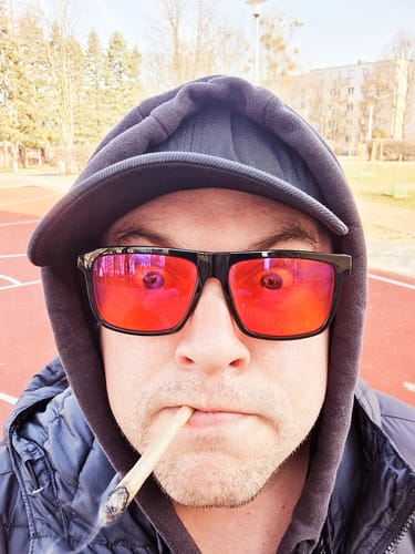 Customer wearing sunglasses and a hoodie, smoking a joint made from CALI MIX AAA+ outdoors.