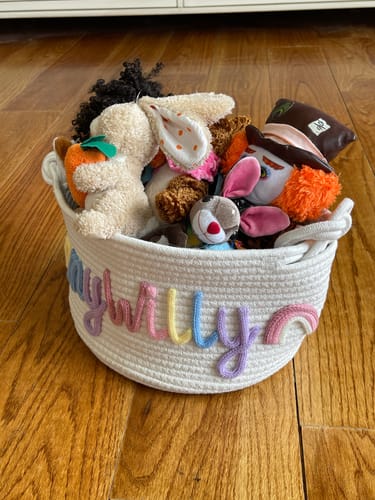 Customer's personalized Baby Knits™ basket with a rainbow name and icon, filled with toys on a wooden floor.