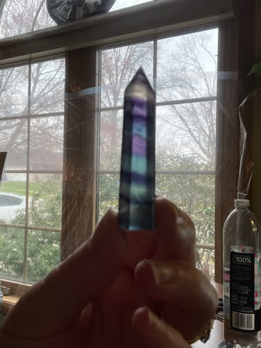 Customer holding a striped rainbow fluorite crystal point up to a window to show its colorful bands.