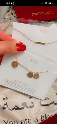 Customer holding up the gold-colored Happiness Necklace in its packaging, showing the three delicate circular pendants.