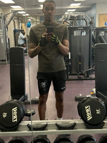 Reviewer's photo of a person taking a mirror selfie in a gym, associated with a review for the SAVD Blackout Snapback.